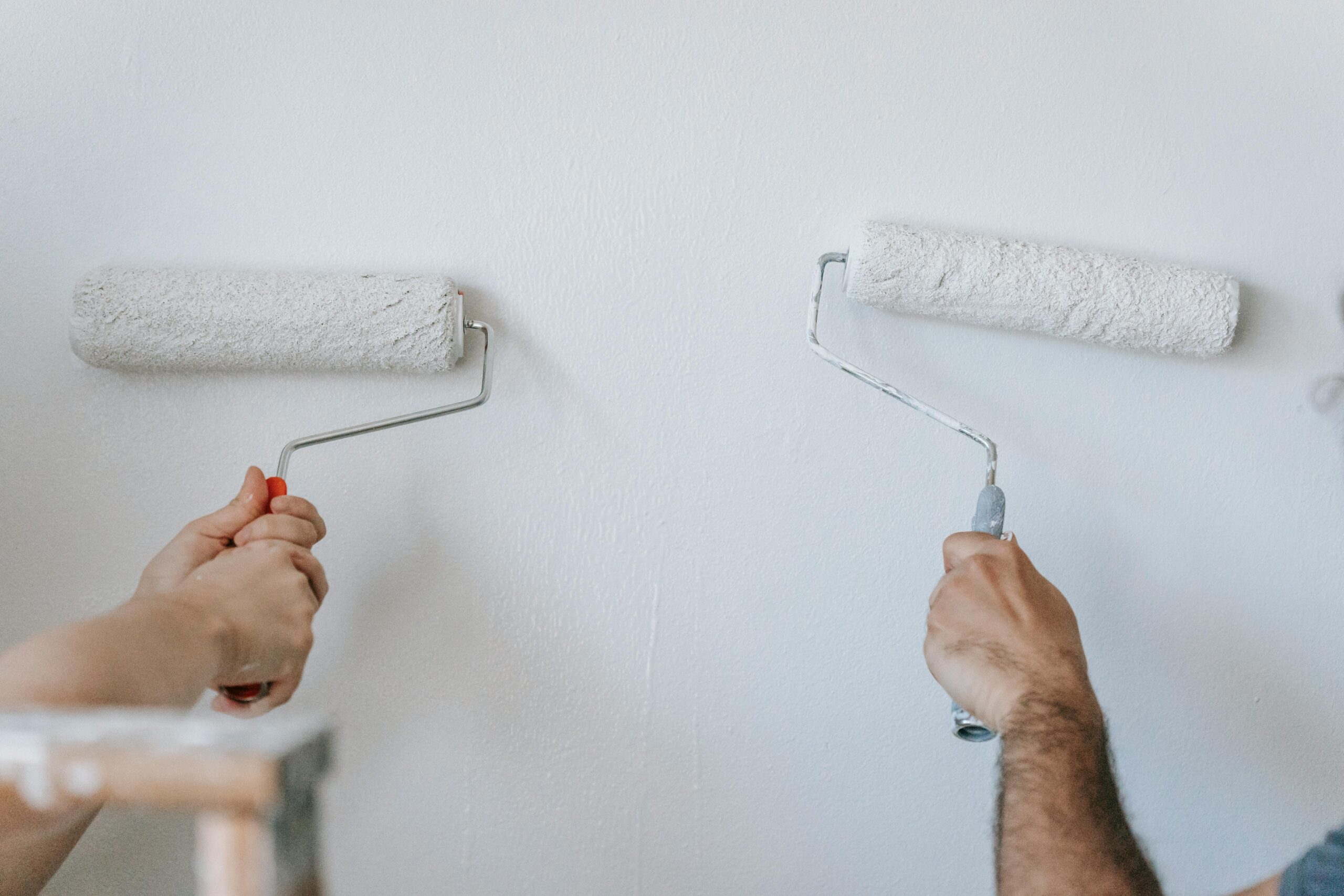two hands holding paint rollers up to wall